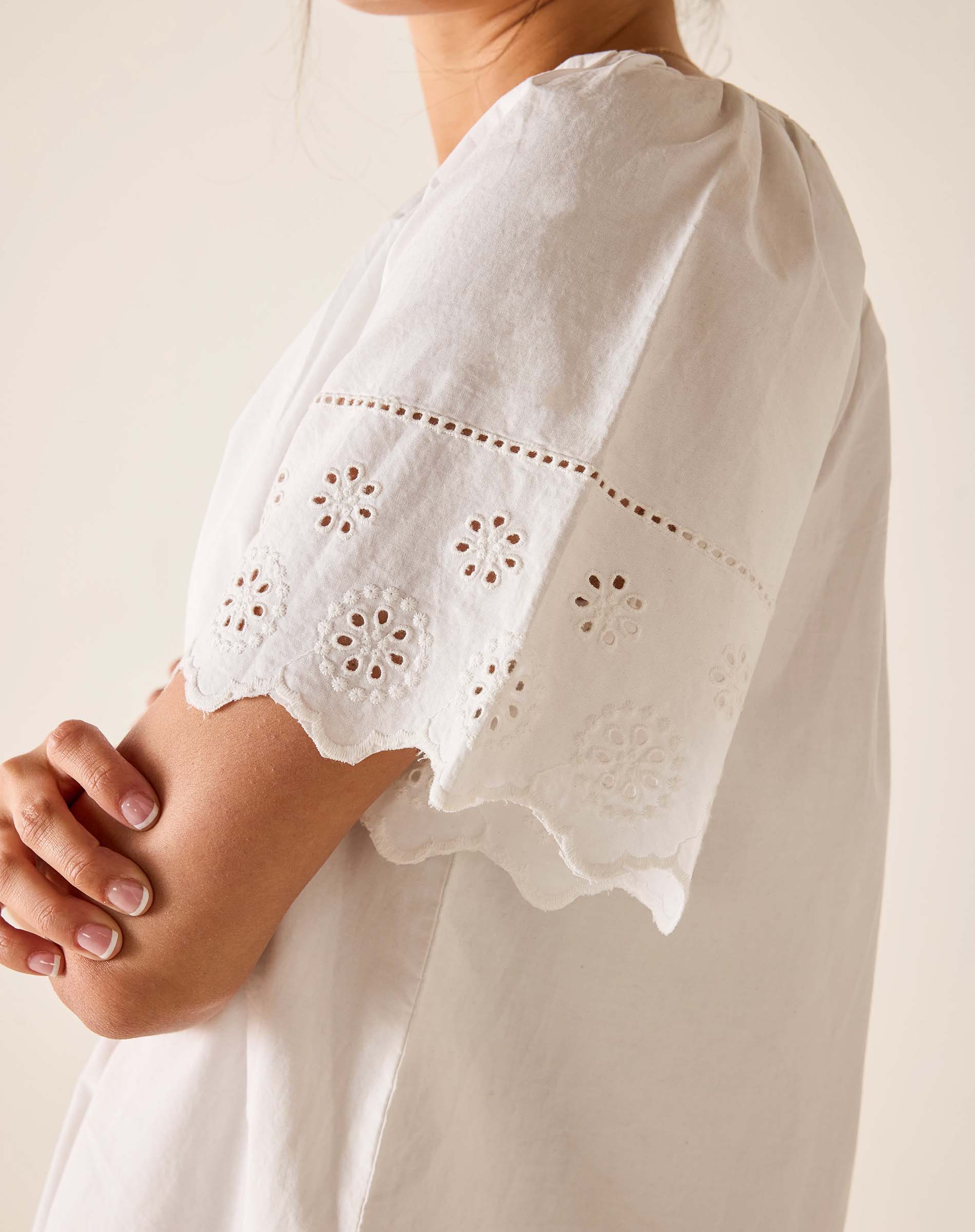 White dress with intricate cut-out patterns on sleeves against a neutral background