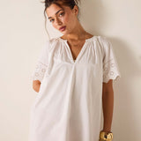 Woman wearing a white dress with lace details against a plain background