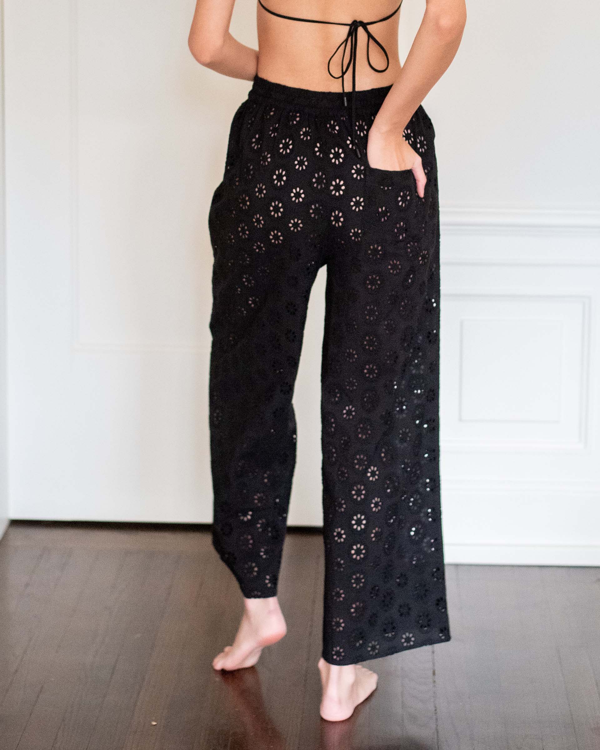 rear view of woman wearing daisy eyelet pant in black with hand in back pocket