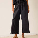 Person wearing black wide-leg pants with lace details on a plain background