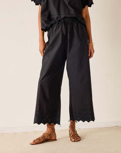 Person wearing black wide-leg pants with lace details on a plain background