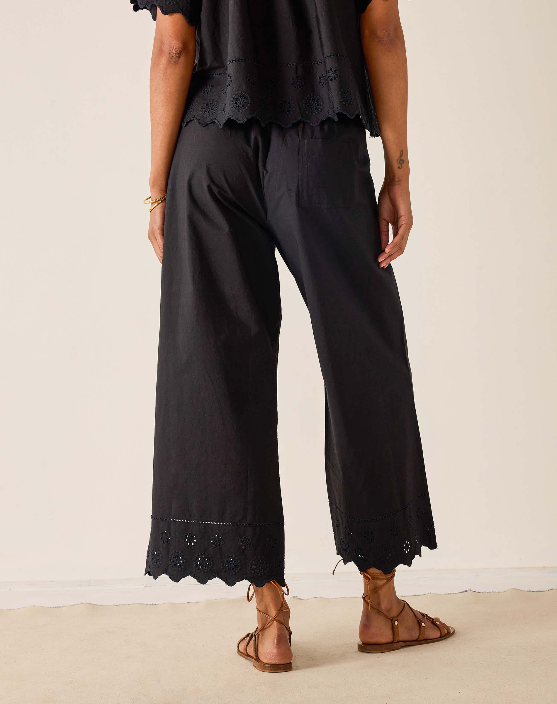 Person wearing black pants with lace details on a beige background