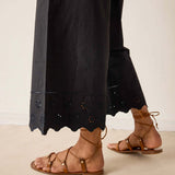 Person wearing black pants with eyelet details and brown sandals on a neutral background