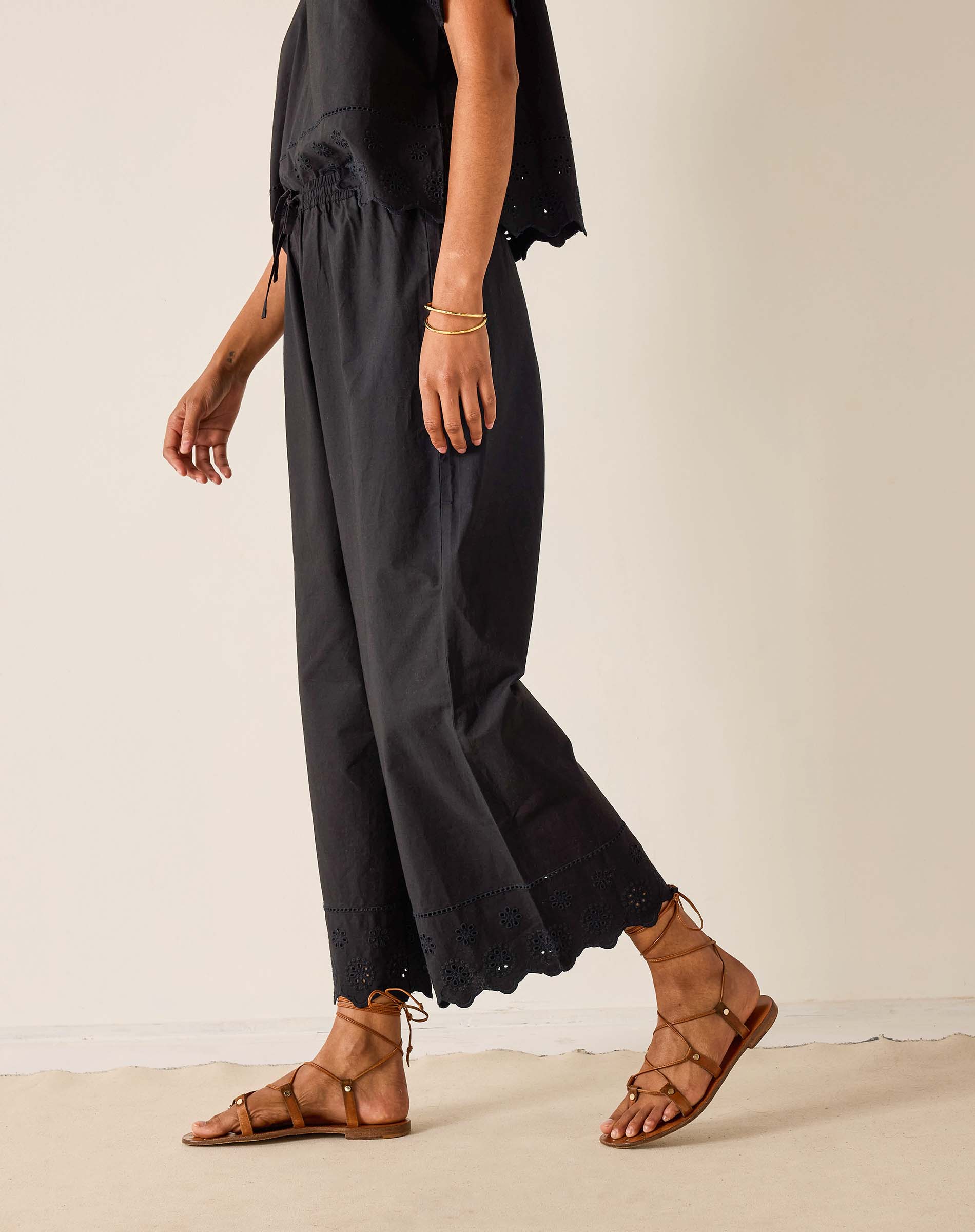 Person wearing black pants and brown sandals on a plain background