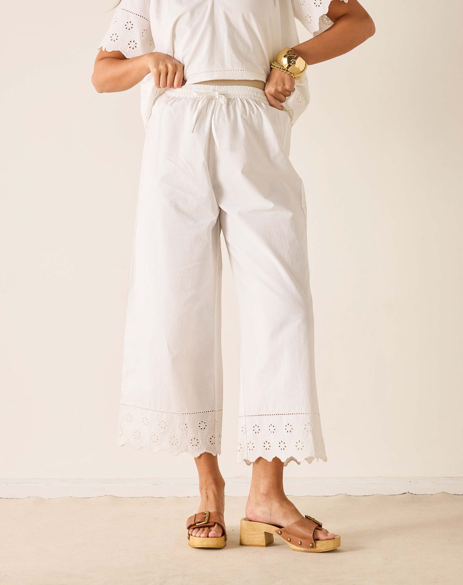Person wearing a white outfit with embroidered details on a plain background