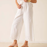 Person wearing a white outfit with lace details and gold sandals on a plain background
