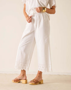 Person wearing a white outfit with lace details and gold sandals on a plain background