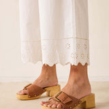 Brown wooden clogs worn with a white lace dress on a neutral background