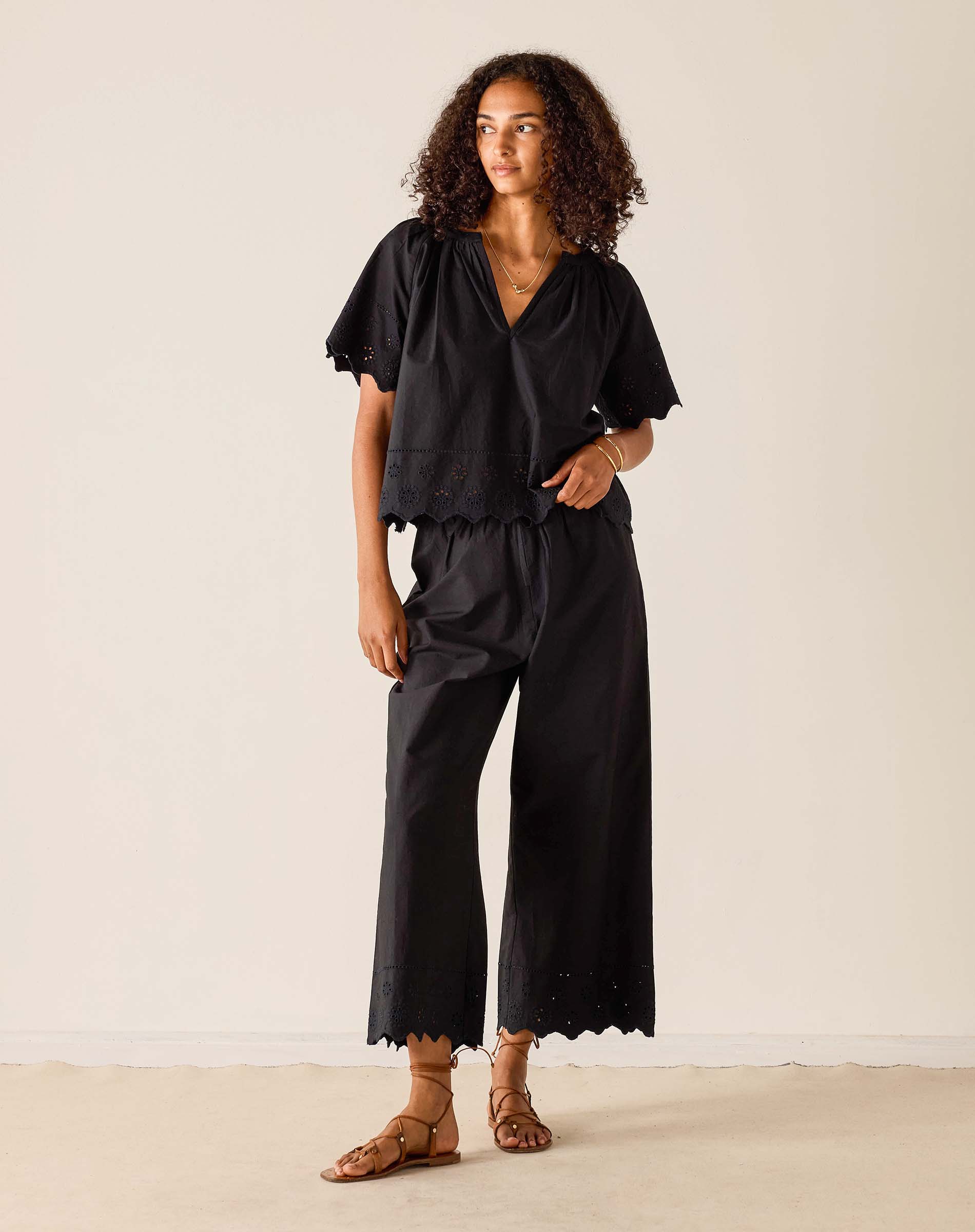 Woman wearing a black outfit with wide-leg pants against a plain background