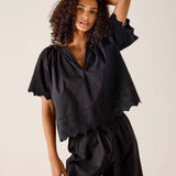 Woman wearing a black blouse with ruffled sleeves against a beige background