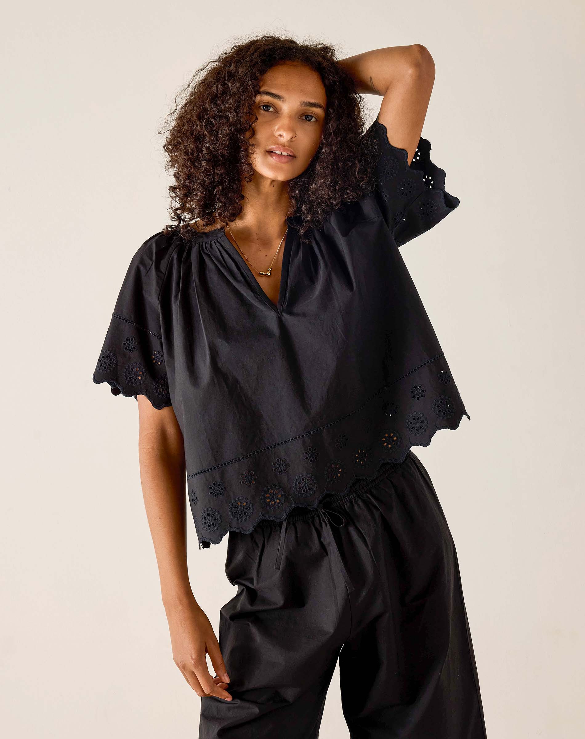 Woman wearing a black blouse with ruffled sleeves against a beige background