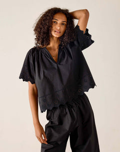 Woman wearing a black blouse with ruffled sleeves against a beige background