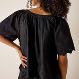 Person wearing a black blouse with intricate cut-out details on a plain background