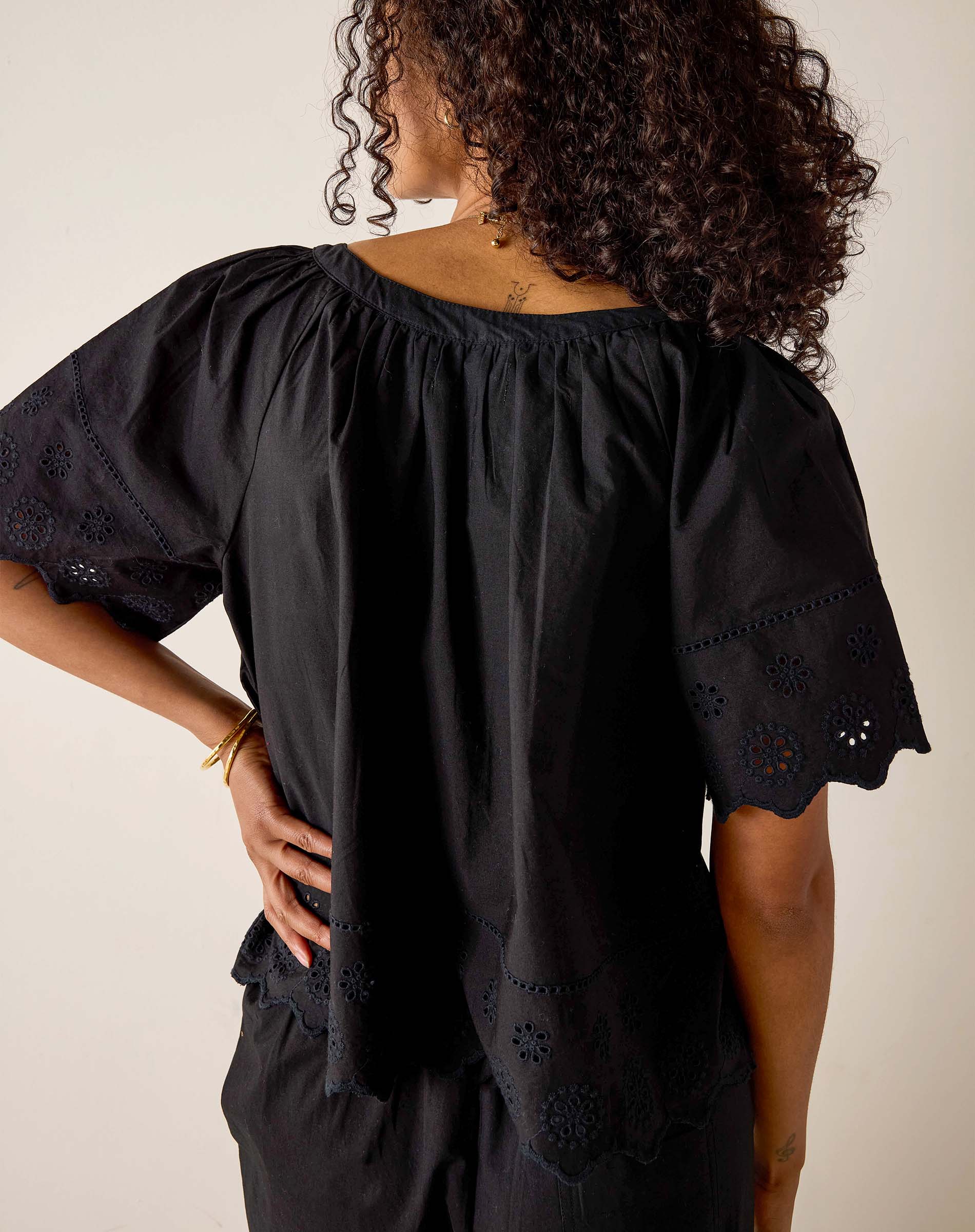 Person wearing a black blouse with intricate cut-out details on a plain background