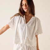 Woman wearing a white embroidered top and pants against a plain background
