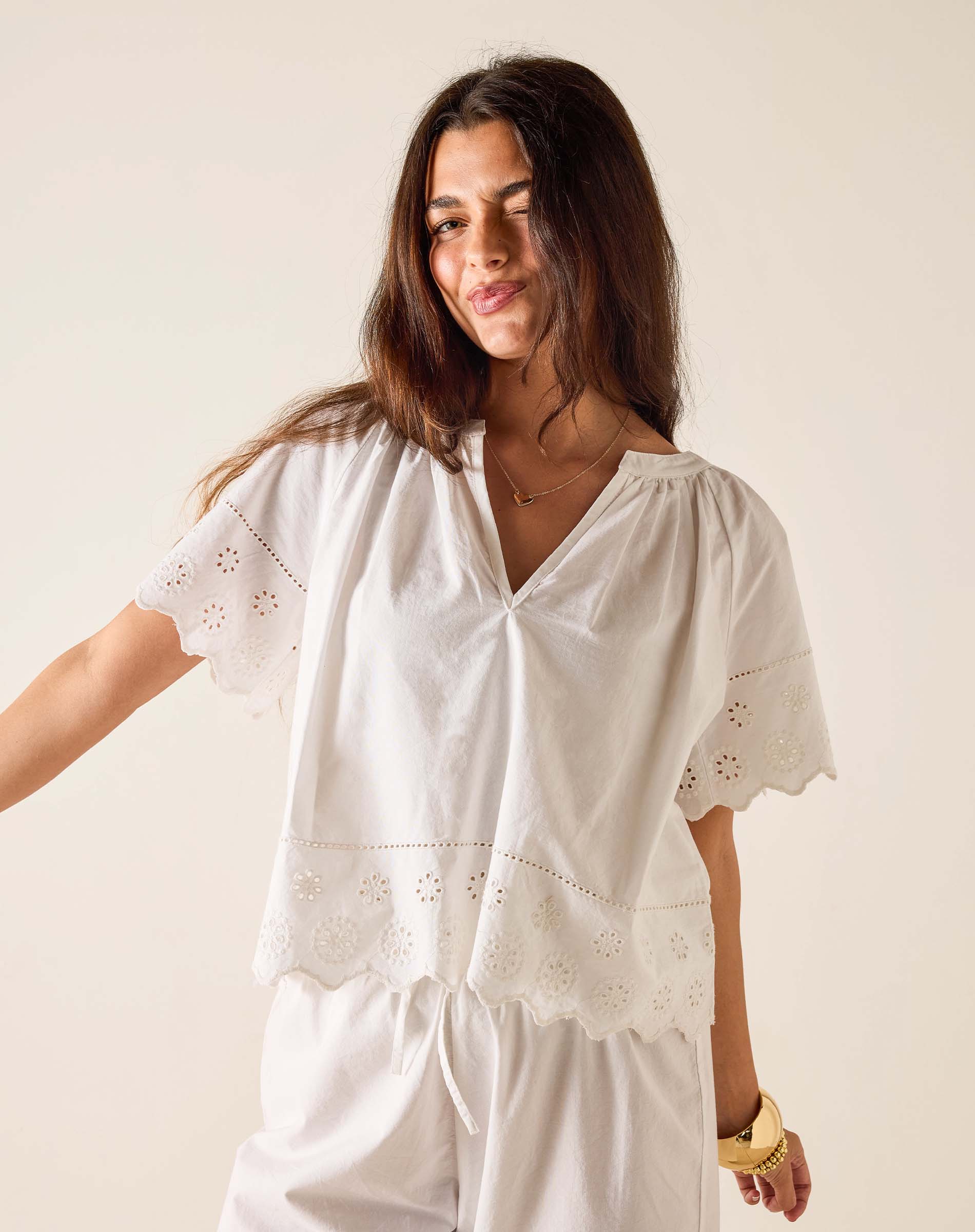 Woman wearing a white embroidered top and pants against a plain background