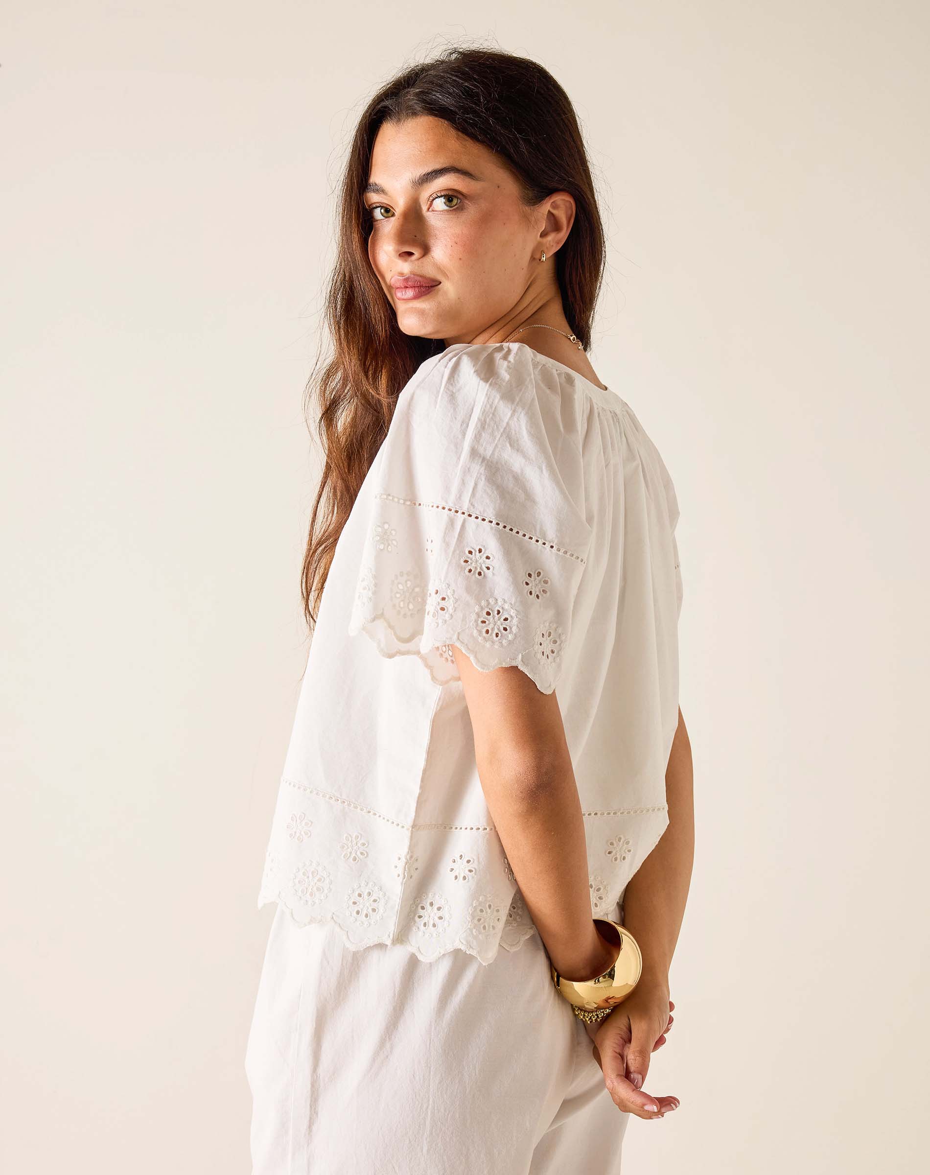 Woman wearing a white blouse with intricate patterns on a plain background