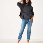 Person wearing a dark gray sweater, blue jeans, and a patterned cap on a white background
