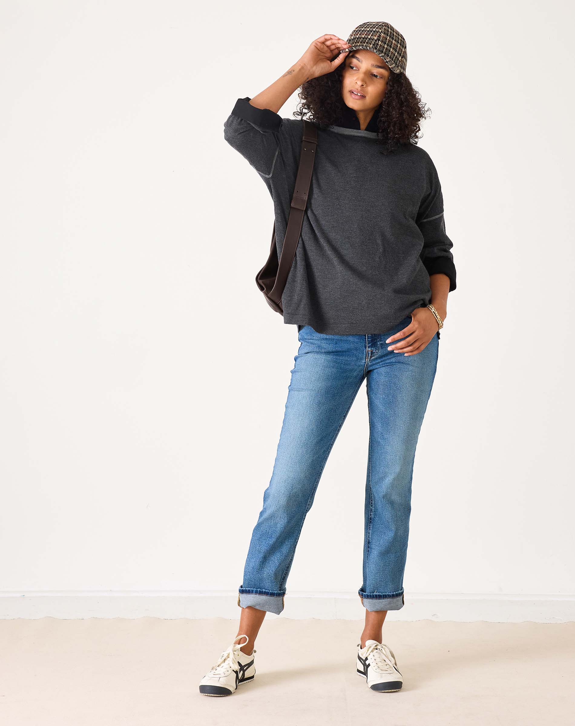 Person wearing a dark gray sweater, blue jeans, and a patterned cap on a white background