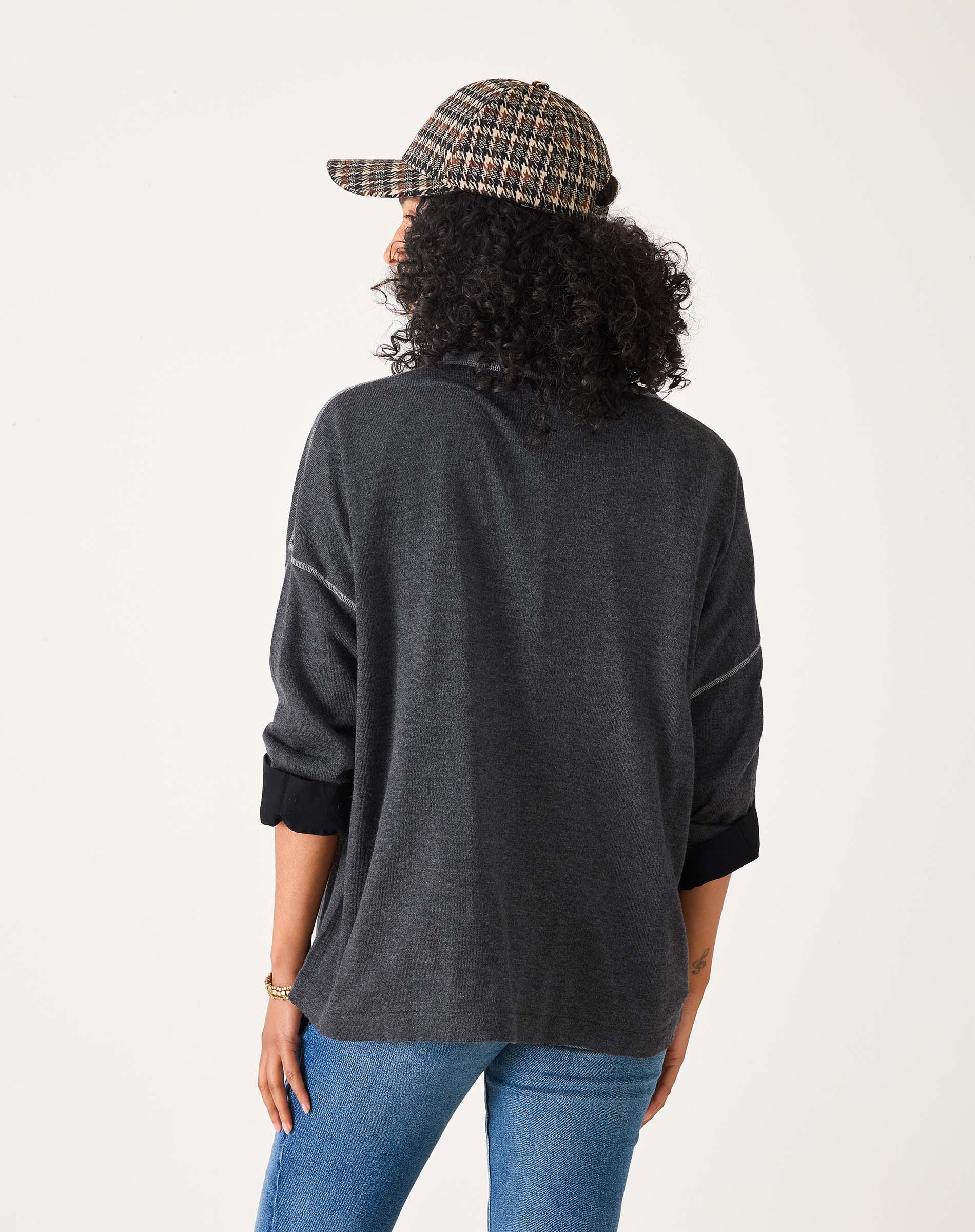 Person wearing a dark gray long-sleeve shirt and blue jeans with a plaid cap on a white background