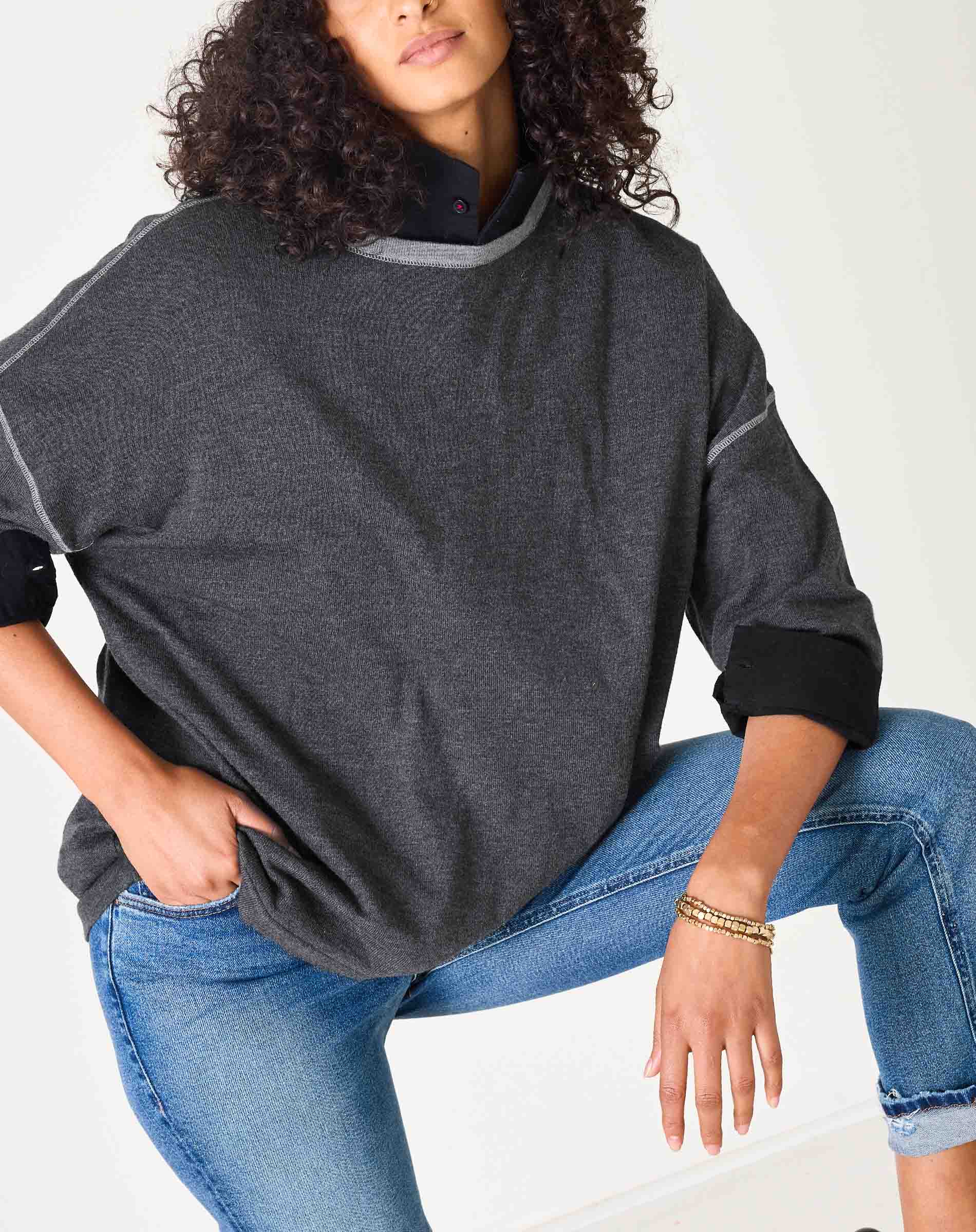 Person wearing a dark gray sweater and blue jeans on a white background
