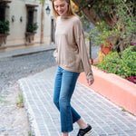 Woman walking on a cobblestone street wearing a beige sweater and blue jeans.