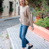 Woman walking on a cobblestone street wearing a beige sweater and blue jeans.