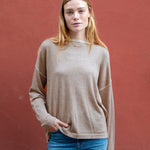 Woman wearing a beige sweater and blue jeans against a red background