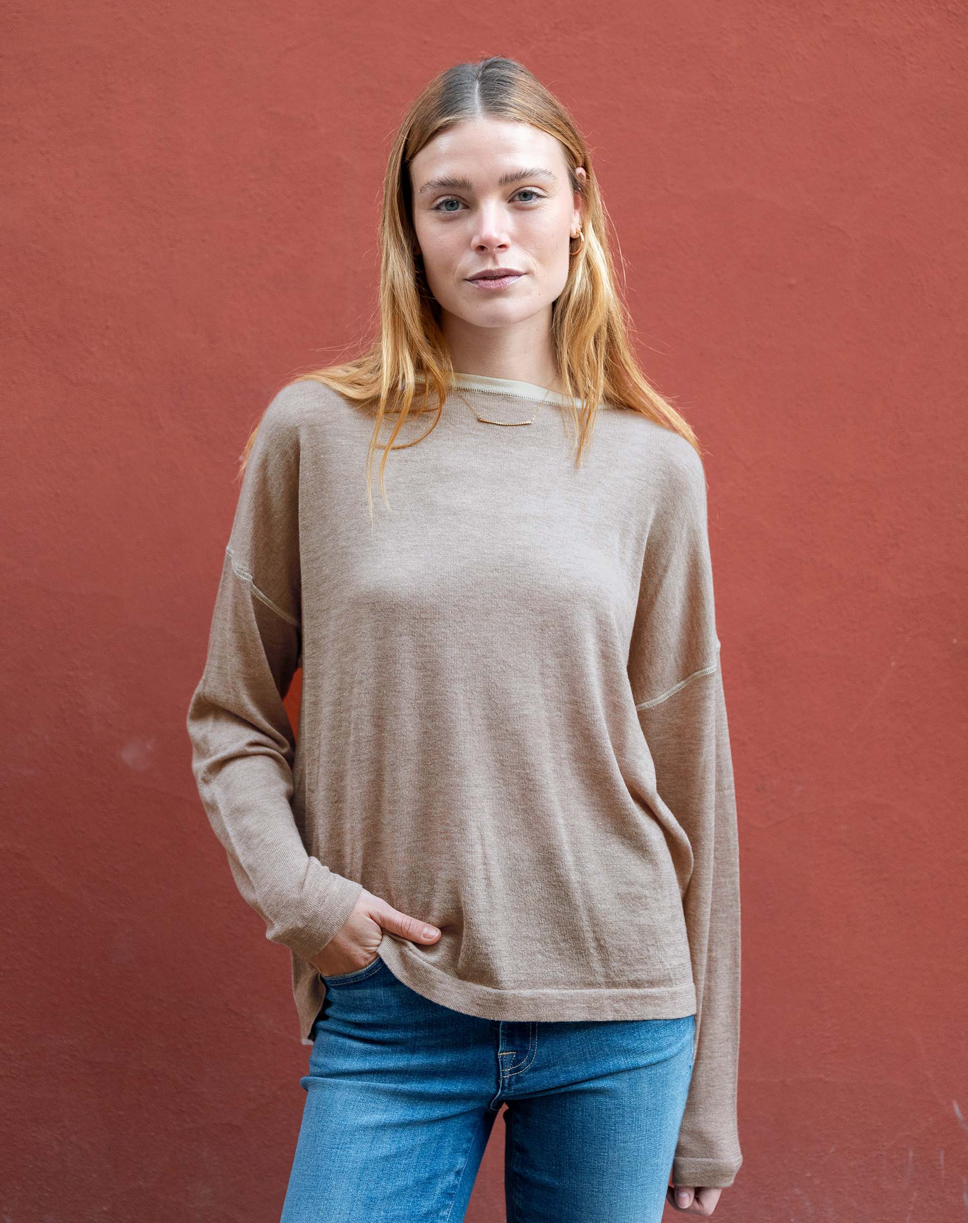 Woman wearing a beige sweater and blue jeans against a red background
