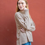 Woman wearing a beige sweater and blue jeans against a red background