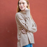 Woman wearing a beige sweater and blue jeans against a red background
