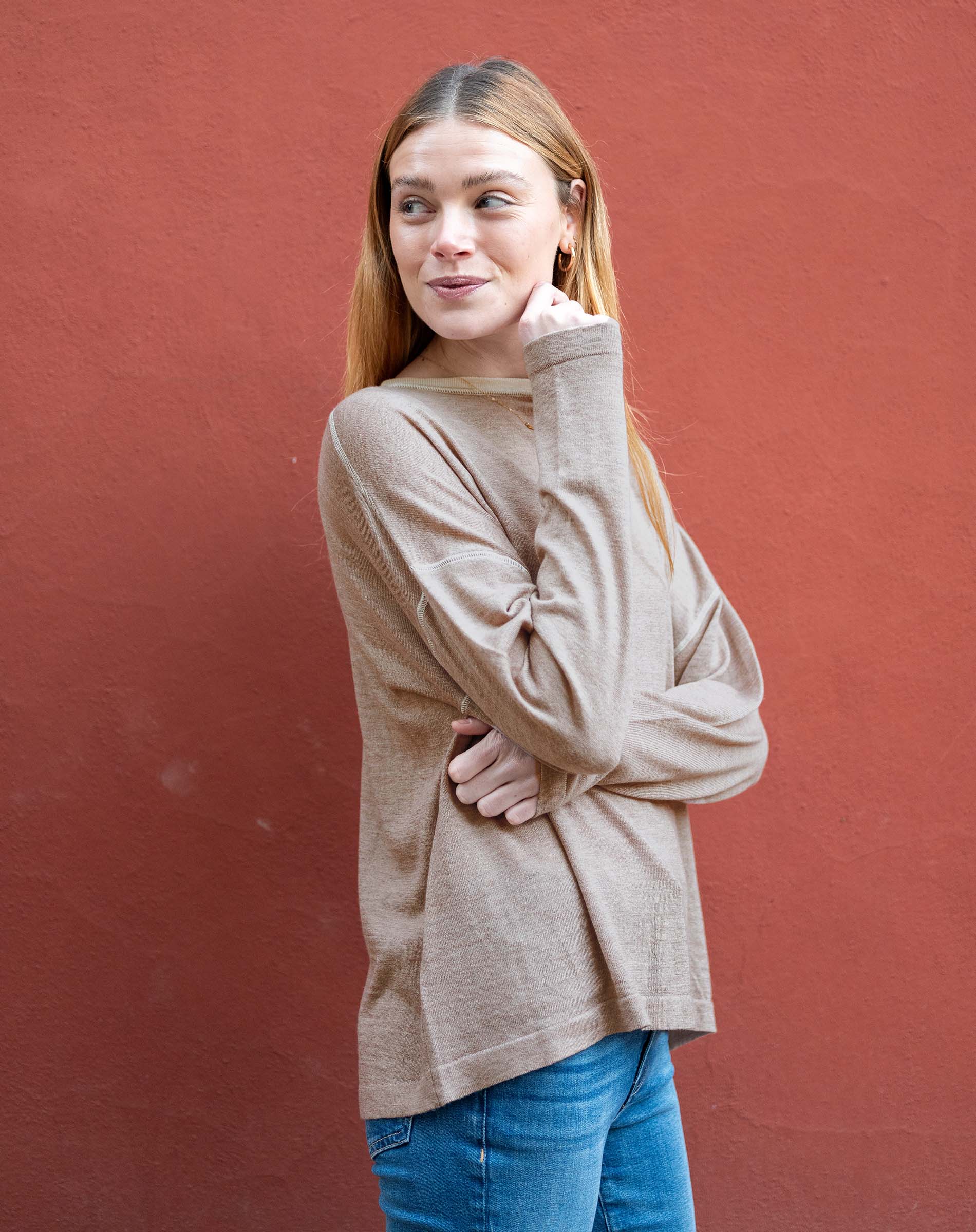 Woman wearing a beige sweater and blue jeans against a red background