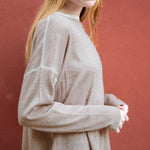 Person wearing a beige long-sleeve shirt against a red background