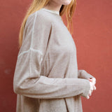 Person wearing a beige long-sleeve shirt against a red background