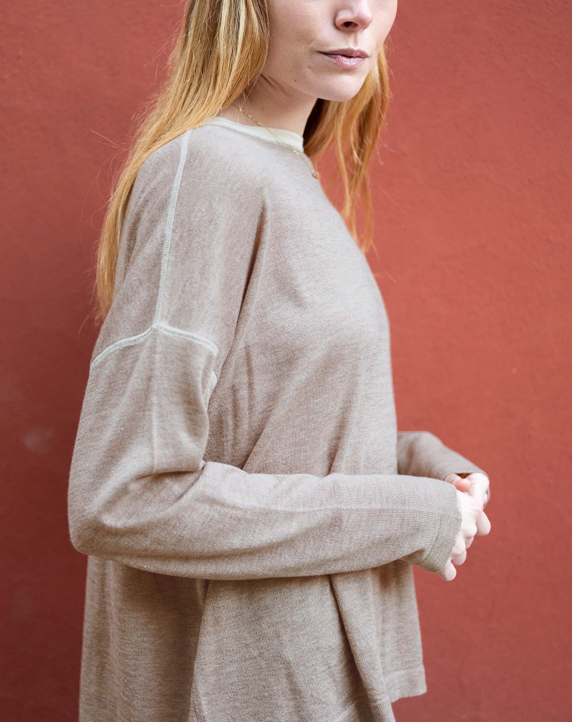 Person wearing a beige long-sleeve shirt against a red background