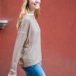 Woman wearing a beige sweater and blue jeans against a red wall