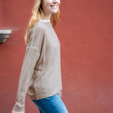 Woman wearing a beige sweater and blue jeans against a red wall