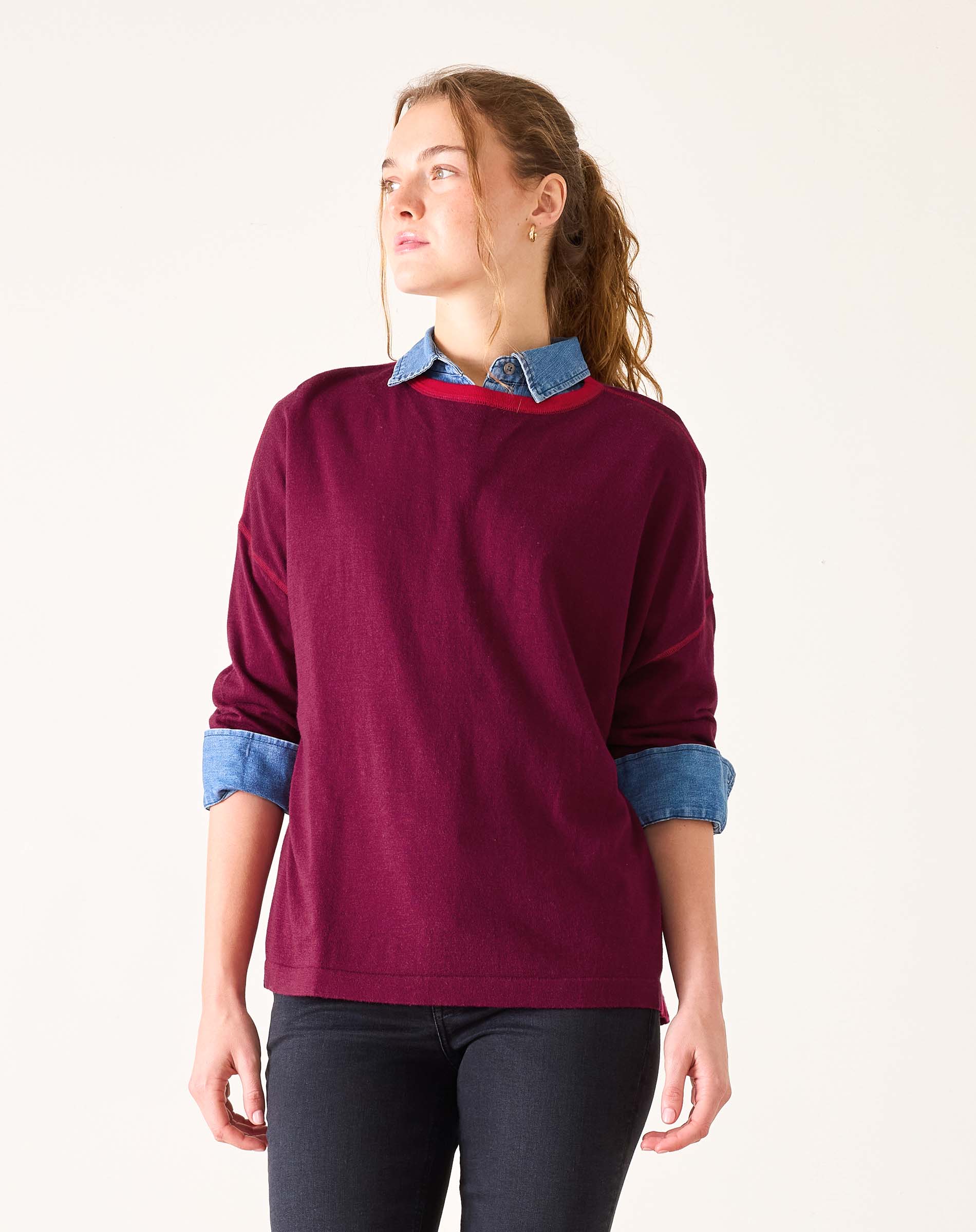 Woman wearing a burgundy sweater with denim collar and cuffs on a white background