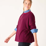 Woman wearing a burgundy sweater with rolled-up denim sleeves on a white background