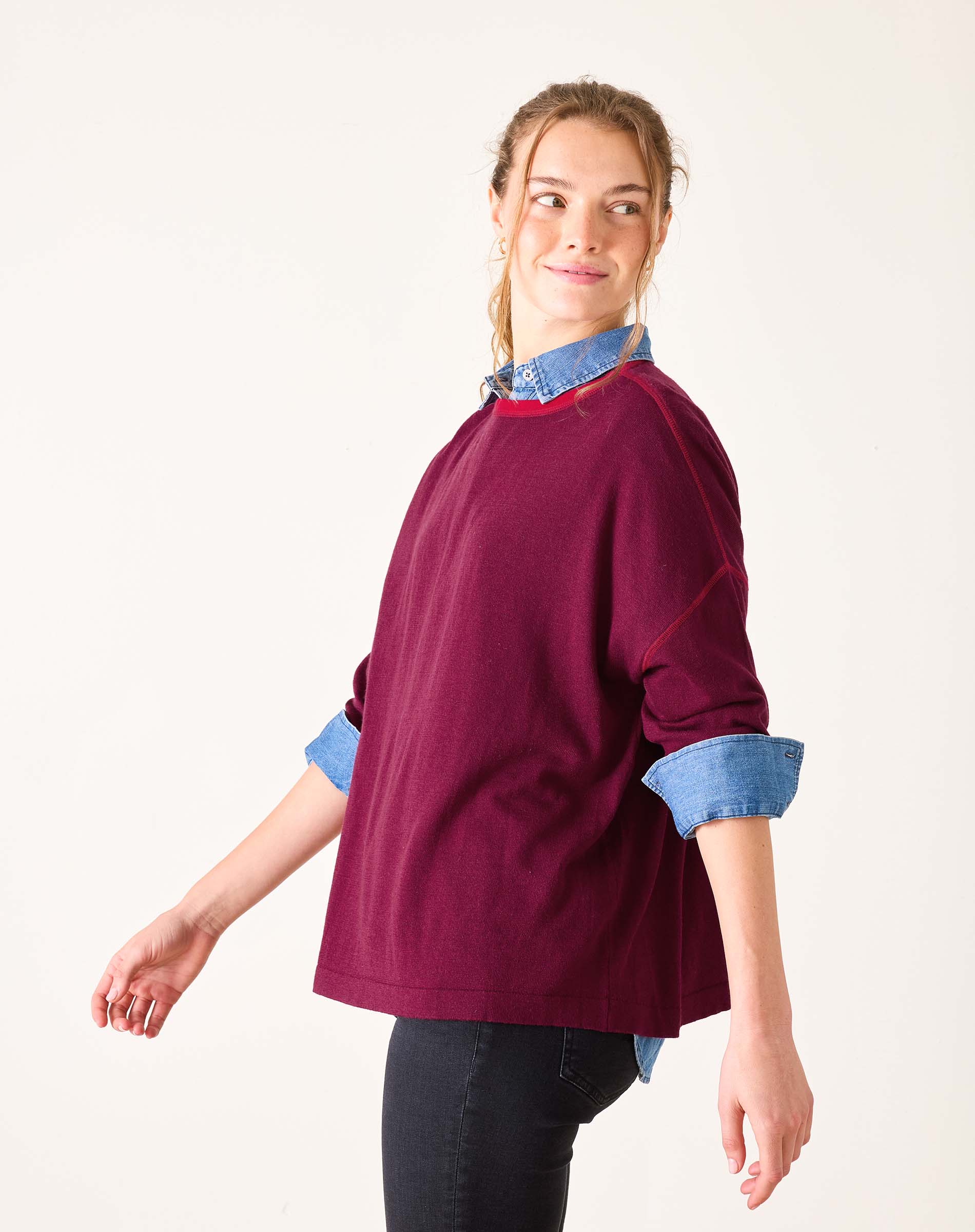 Woman wearing a burgundy sweater with rolled-up denim sleeves on a white background