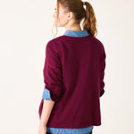 Woman wearing a burgundy sweater with blue collar and cuffs on a white background