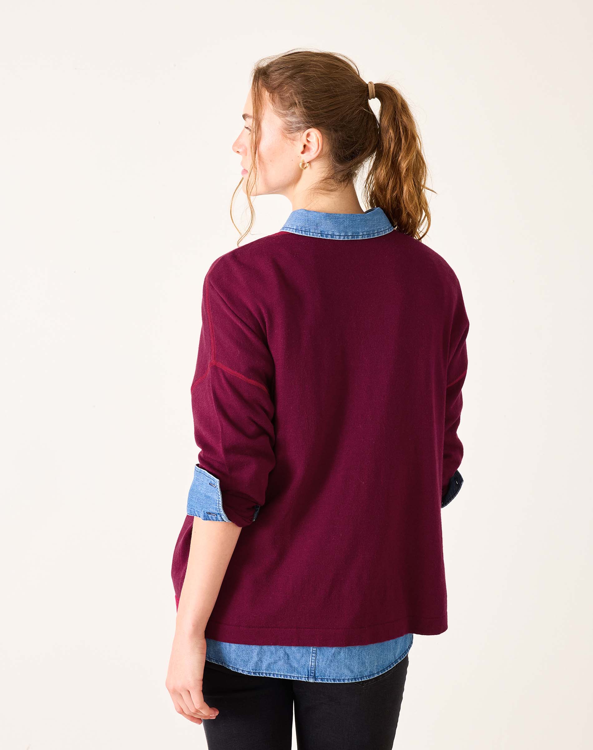 Woman wearing a burgundy sweater with blue collar and cuffs on a white background