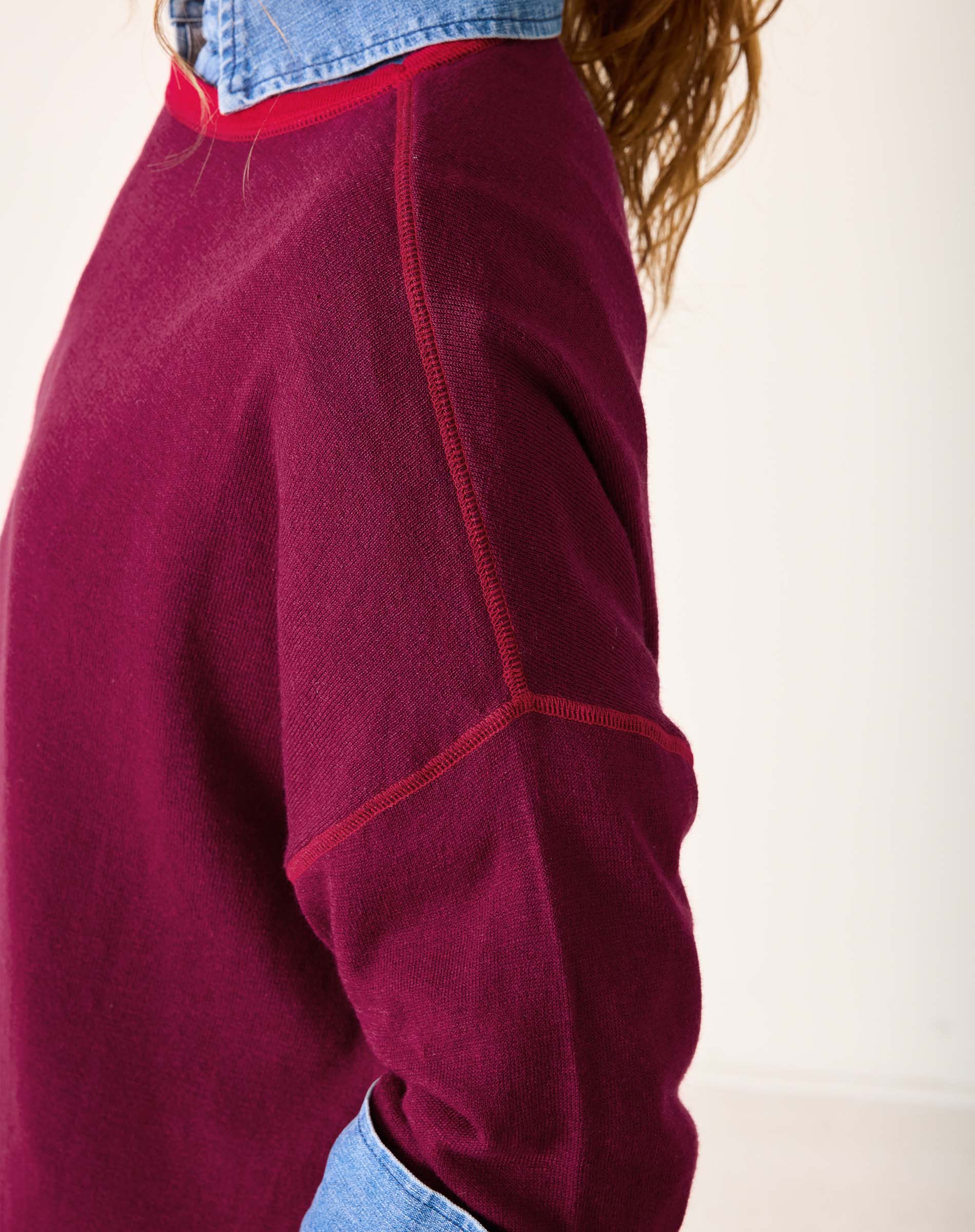 Close-up of a maroon fleece jacket with red stitching on a white background