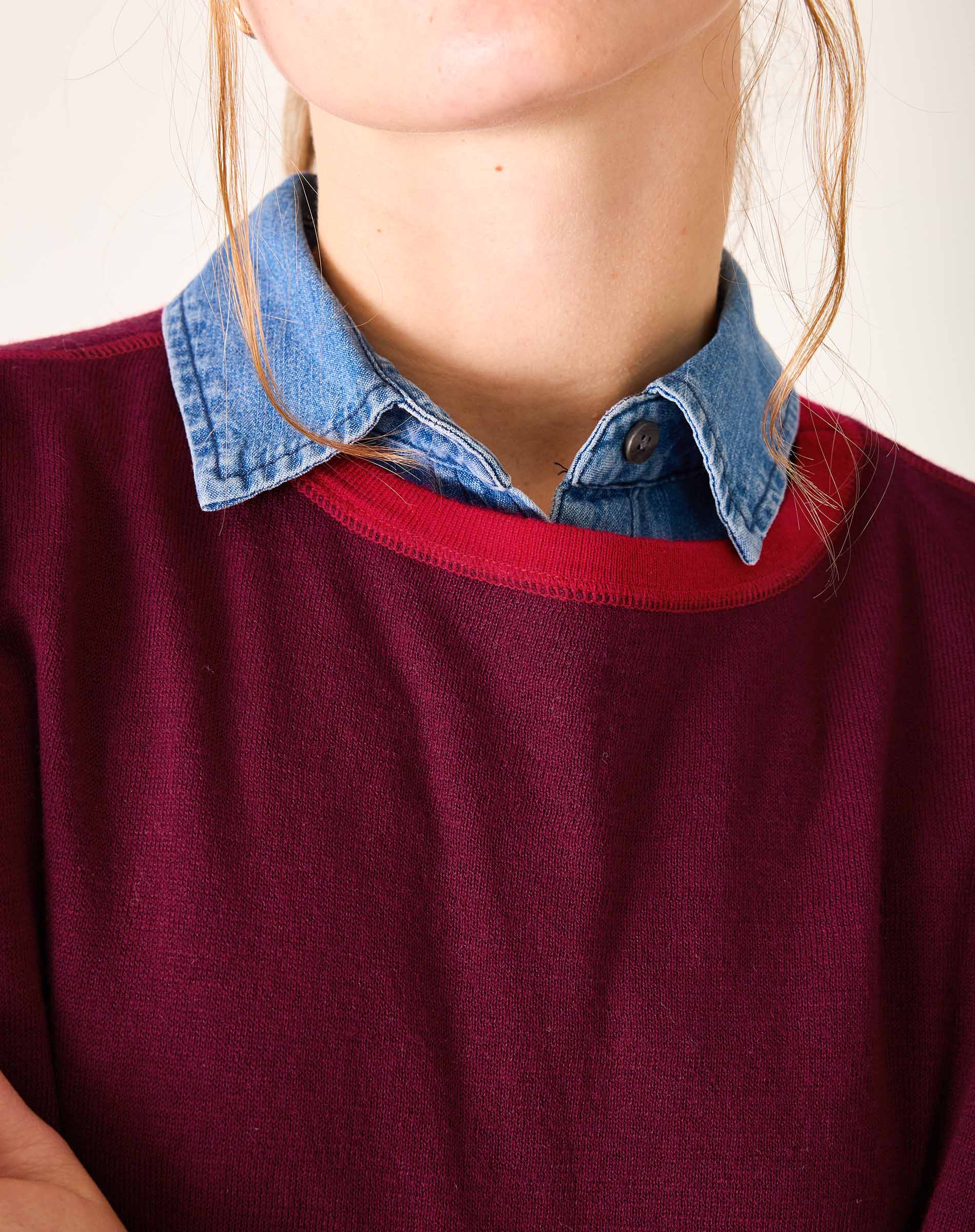 Person wearing a red sweater with a blue collar against a neutral background