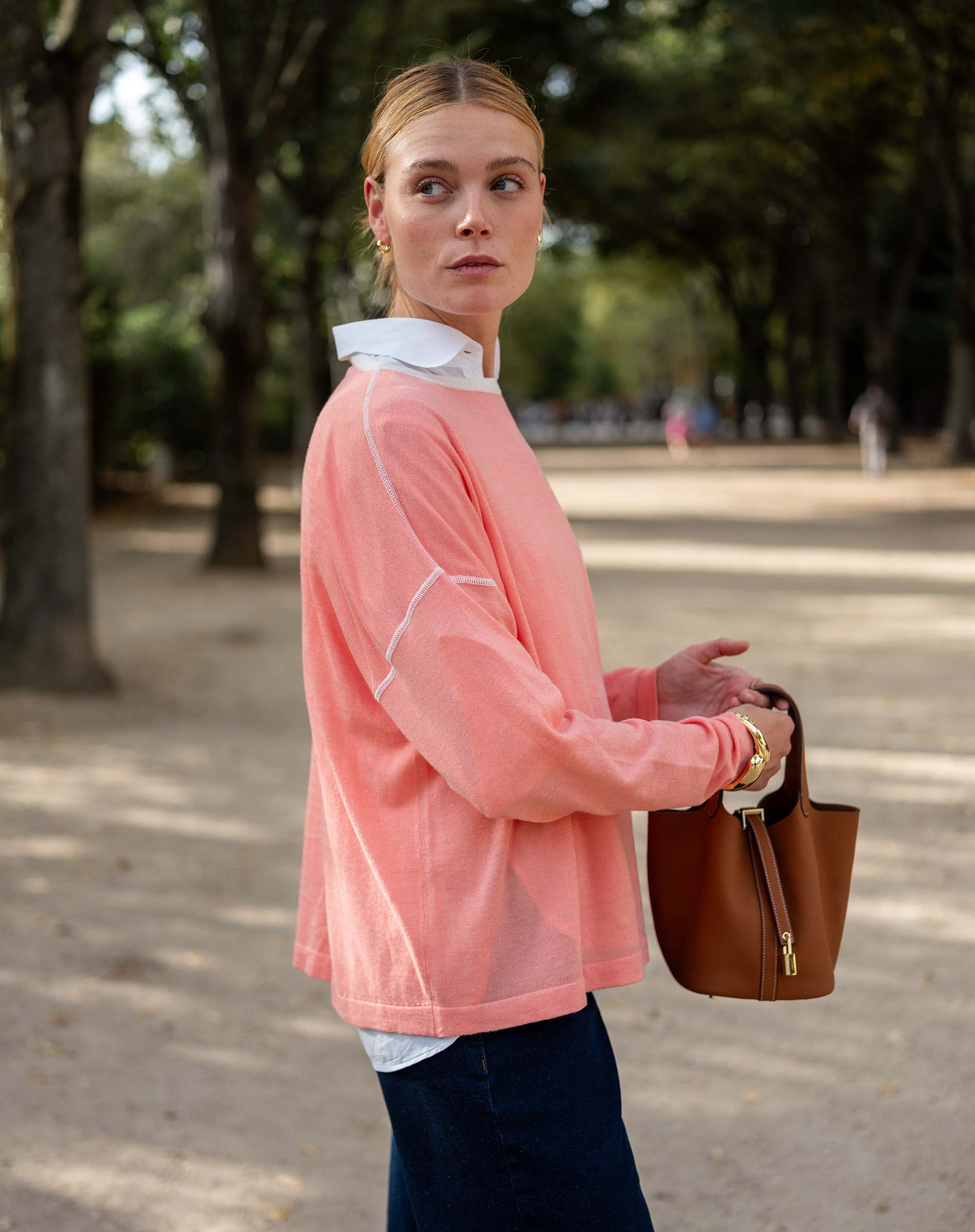 Woman in a pink jacket holding a brown bag outdoors
