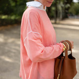 Woman wearing a pink sweater and holding a brown handbag outdoors.