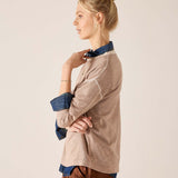 Fawn knit sweater with a layered blue button-down shirt and brown trousers