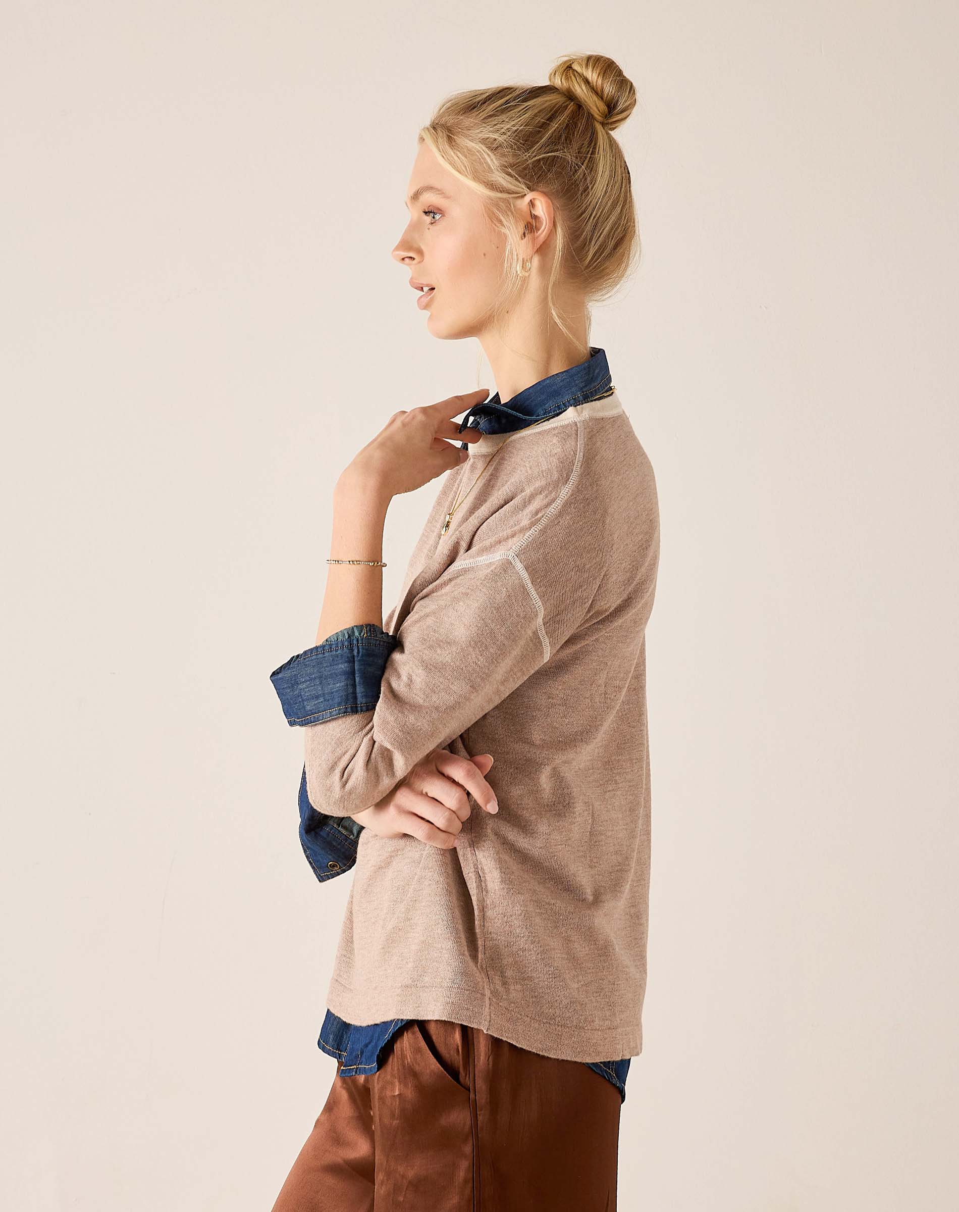 Fawn knit sweater with a layered blue button-down shirt and brown trousers