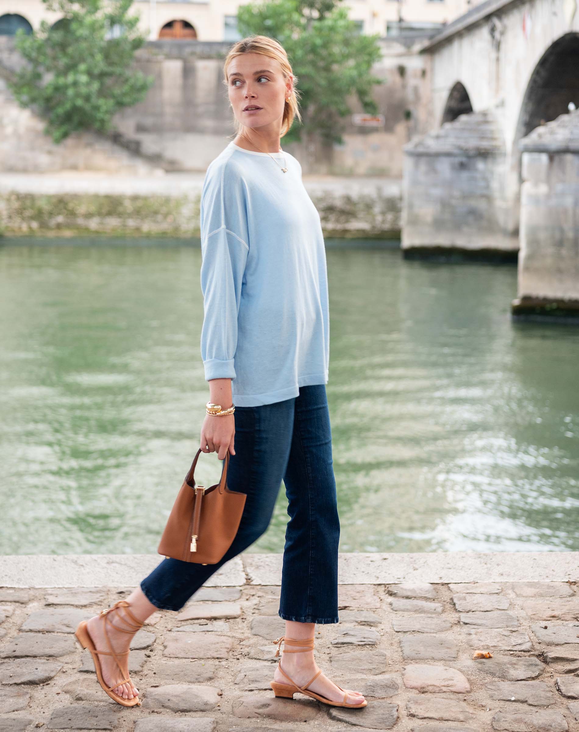 Woman walking by a river with a bridge in the background