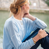 Woman sitting by a waterfront wearing a light blue shirt and dark jeans, with a blurred background.